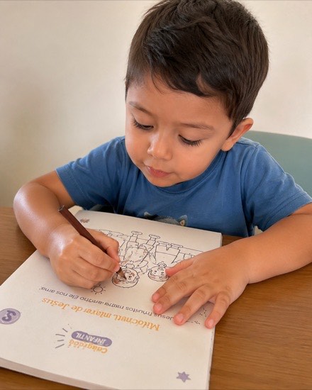 Menino concentrado pintando uma página do material